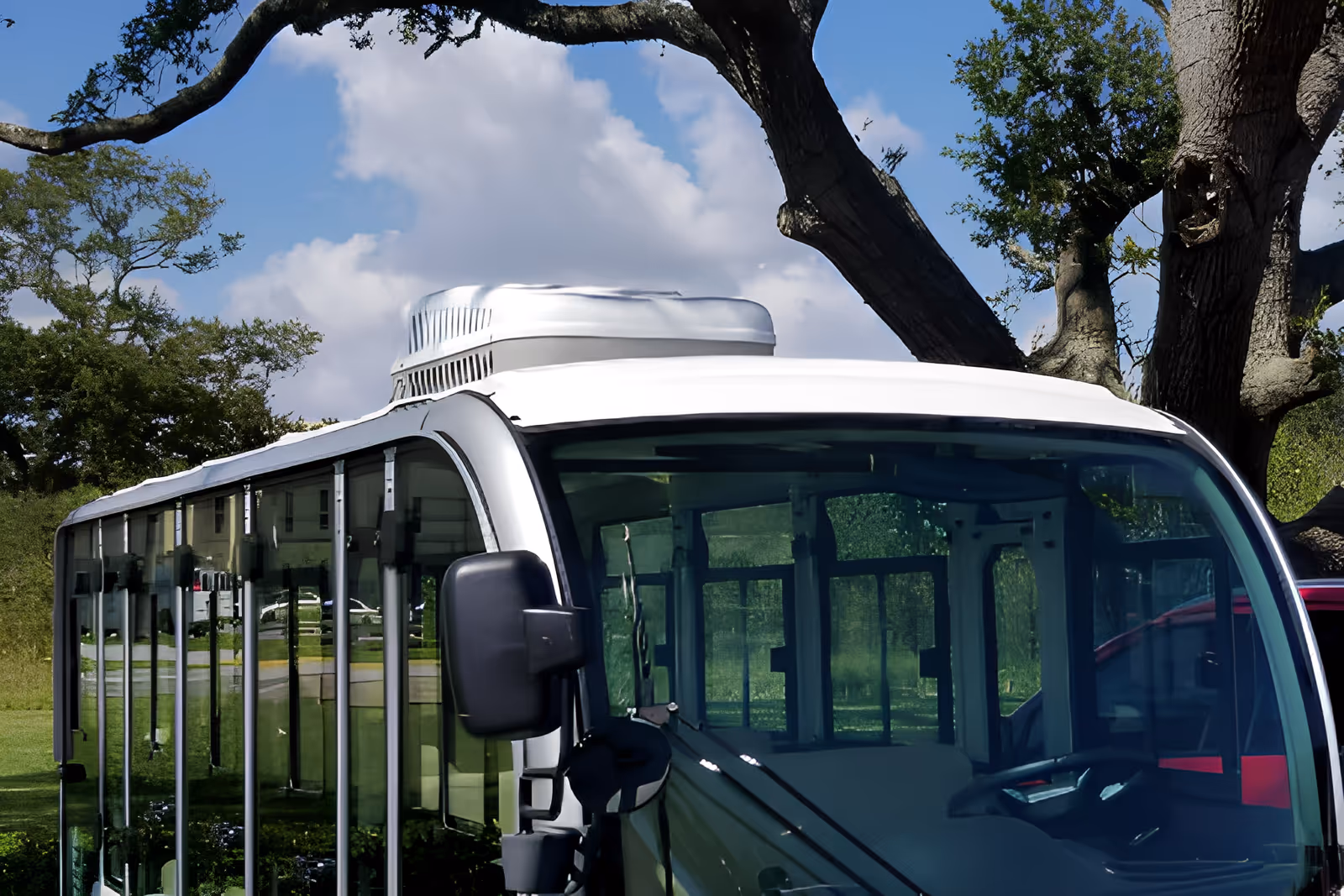 Close-up view of a white shuttle bus parked outdoors with trees and a partly cloudy sky in the background.
