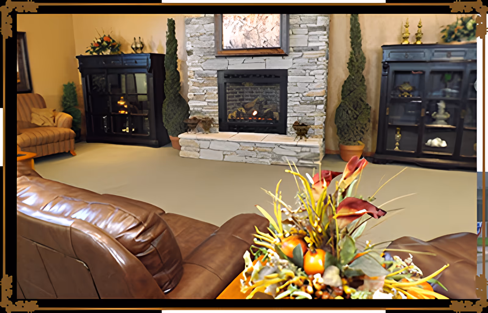 Cozy living room with leather sofas, a stone fireplace flanked by display cabinets, and a floral arrangement in the foreground.