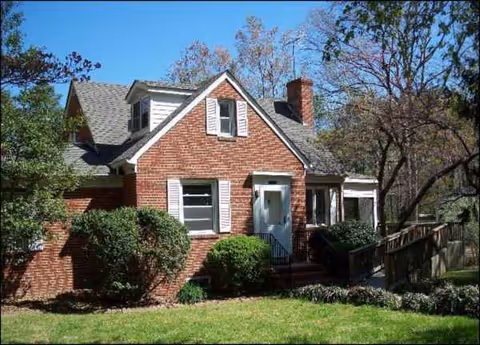 Brick cottage-style senior living home with a front porch, white shutters, and manicured shrubs.