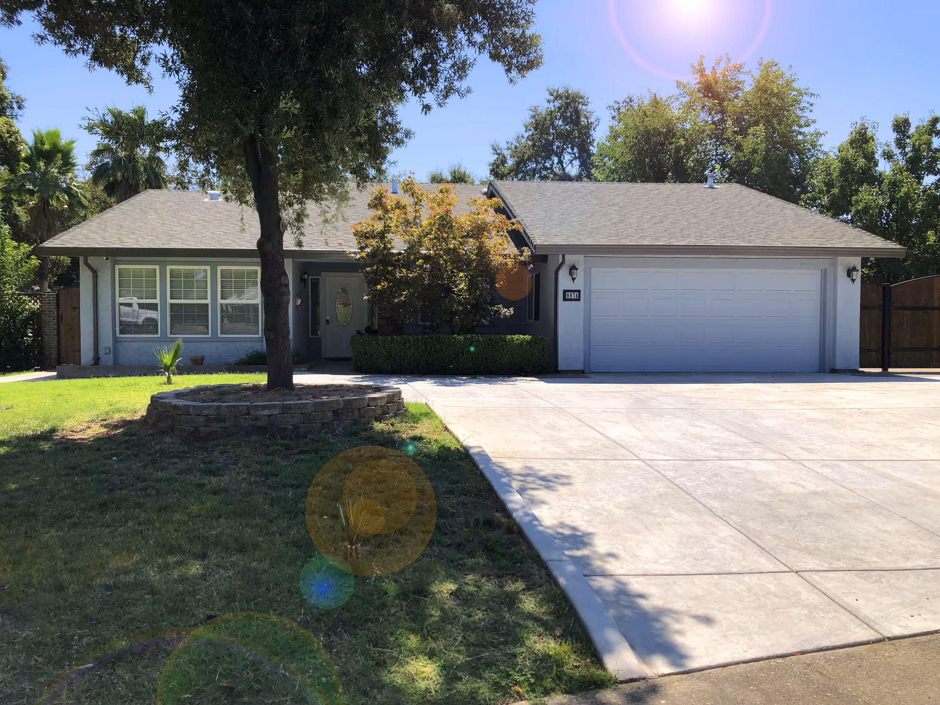 Single-story house with a wide driveway, attached two-car garage, front lawn and trees.