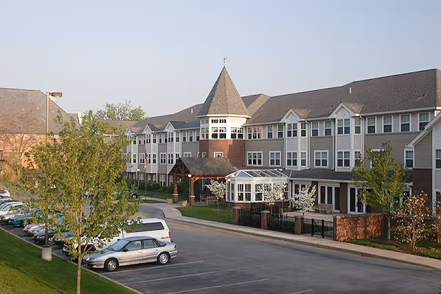Front exterior of a multi-story retirement residence with a turreted entrance, parking lot, and landscaped grounds.