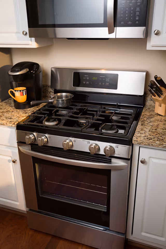Stainless steel gas range and oven beneath a microwave on a granite countertop with a coffee maker and knife block nearby.