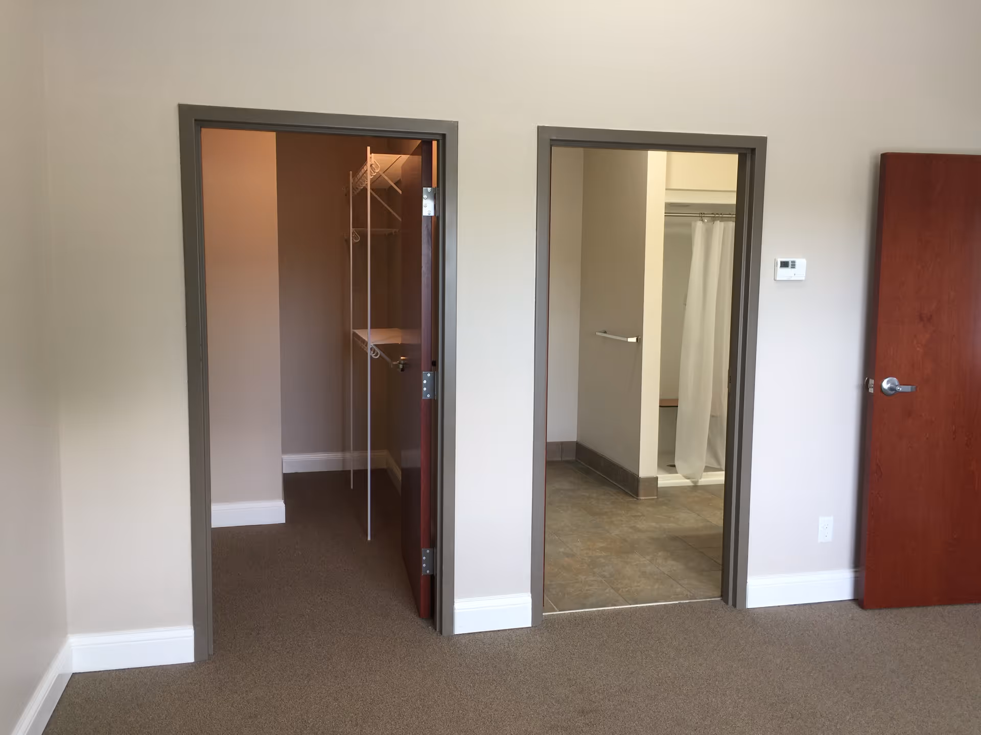 Interior view of a room showing an open closet on the left and an adjoining bathroom with a shower on the right.