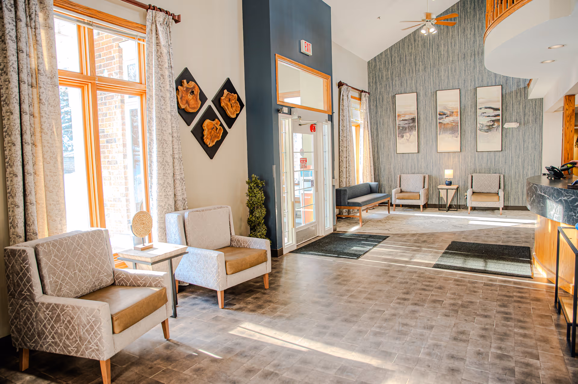 Bright senior living lobby with armchairs, large windows, reception desk, and decorative wall art.