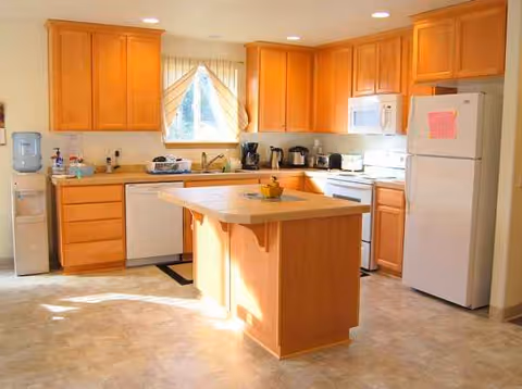 Bright wooden kitchen with island, appliances, and a window with curtains.