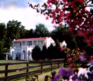 White two-story building with red roof, framed by trees and flowering foreground.