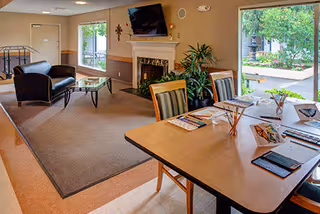 Bright common living area with fireplace, sofas, and a dining table near windows.