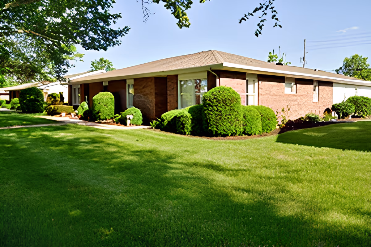Single-story brick building with a manicured lawn and trimmed shrubs under a clear blue sky.