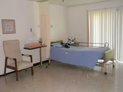 Bedroom in a senior living facility with a bed, chair, and small table.