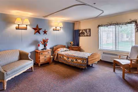 Cozy bedroom in a senior living facility with bed, sofa, dresser, window, and stars.