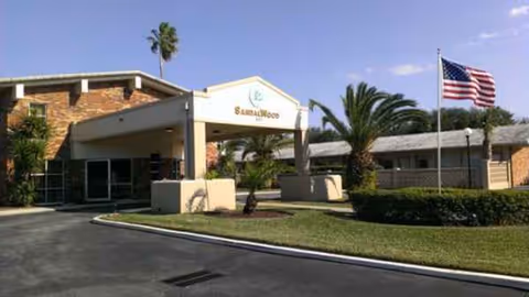 Front exterior of Sandalwood Rehabilitation and Nursing Center with palm trees and an American flag.