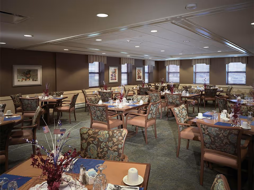 Large dining room with multiple set tables and upholstered chairs and floral centerpieces.