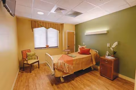 Senior living room with a hospital-style bed, nightstand, chair, and window.