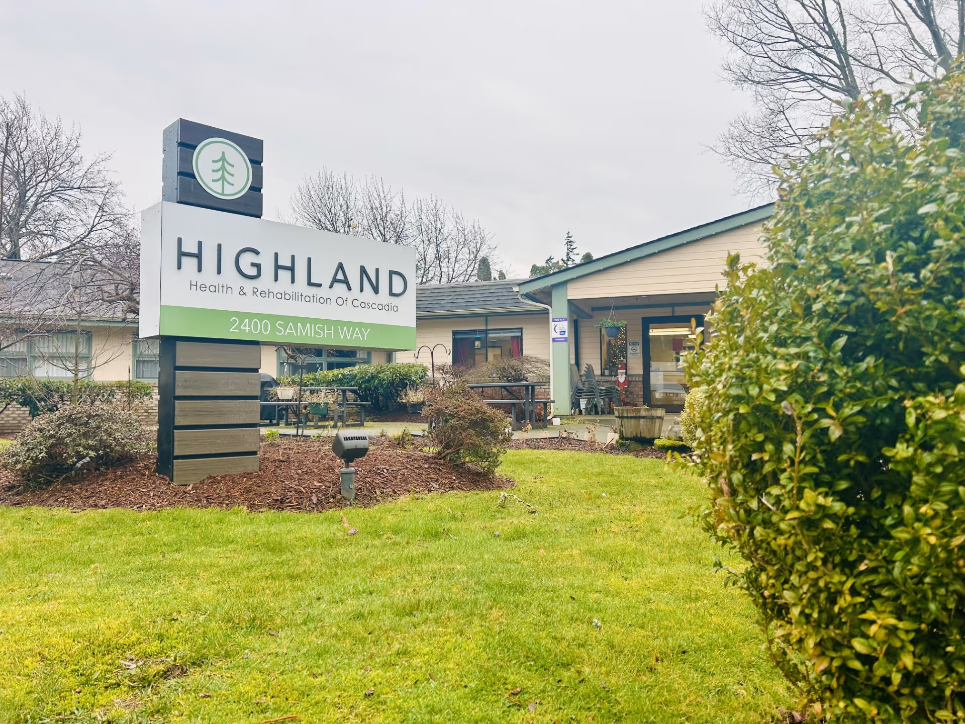 Front sign for Highland Health & Rehabilitation and the facility entrance with lawn and shrubs.