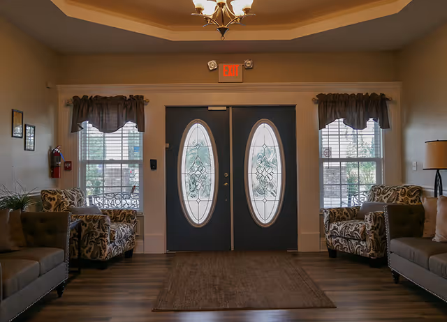 Entrance lobby with double decorative oval-glass doors flanked by windows and upholstered chairs on either side.