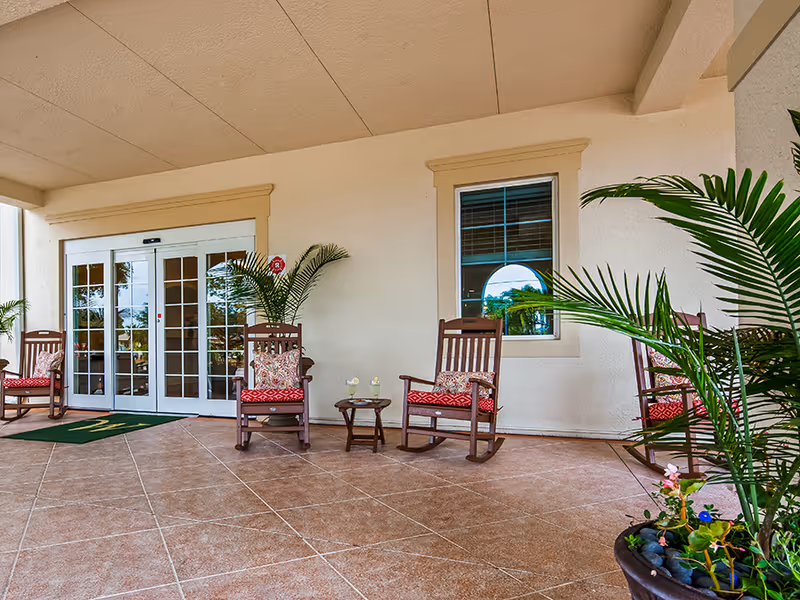 Covered front entrance with wooden rocking chairs, potted plants, and glass double doors.