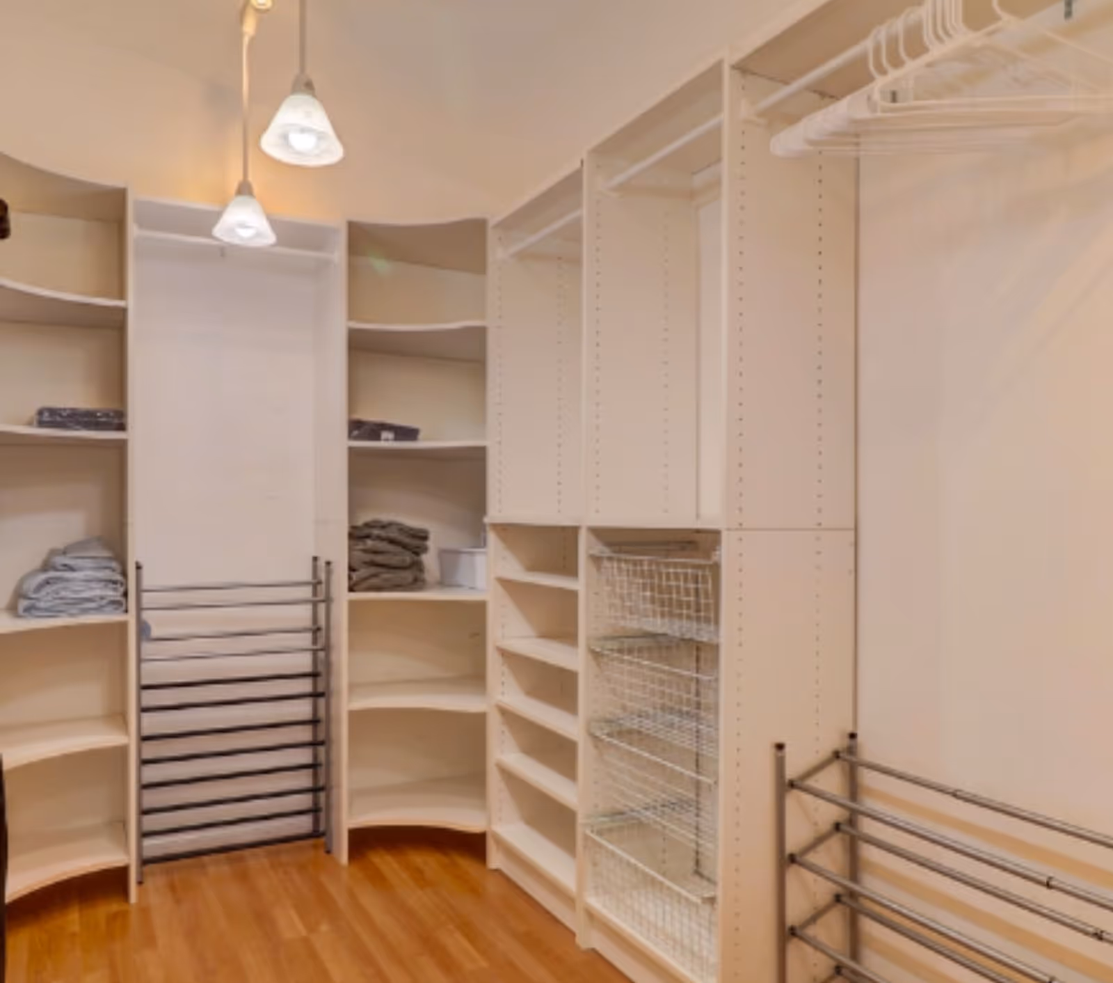 Organized walk-in closet with white built-in shelving, wire baskets, hanging rods, and hardwood flooring.