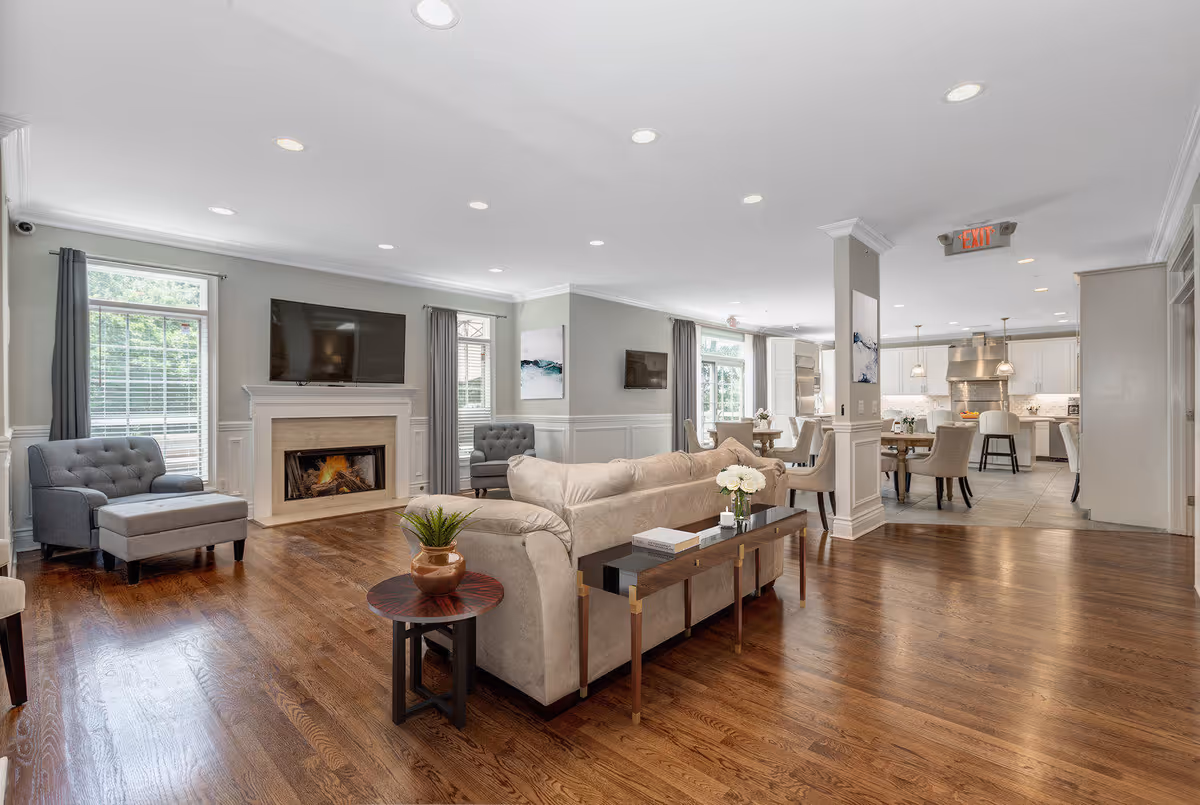 Bright open-concept living room with sofas, a fireplace and TV, leading to a dining area and kitchen in the background.