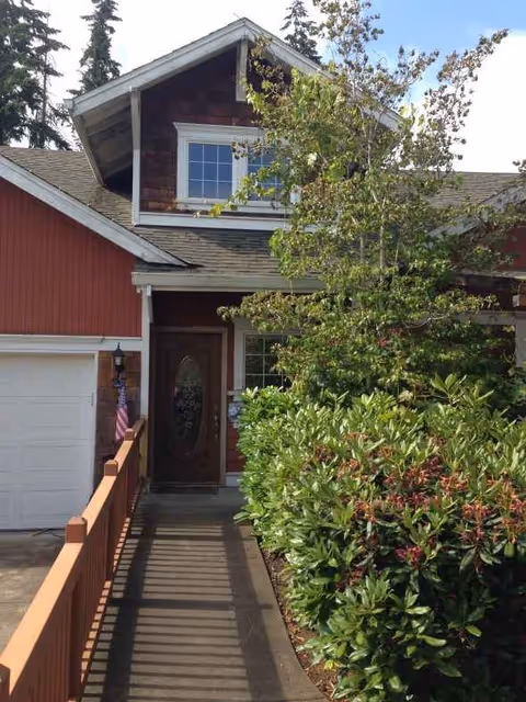 Red exterior of a senior care home with walkway and lush shrubs