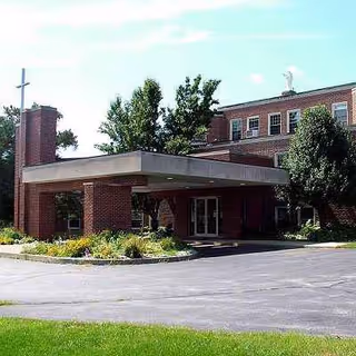 Exterior view of a brick senior living facility entrance with a canopy and landscaping.