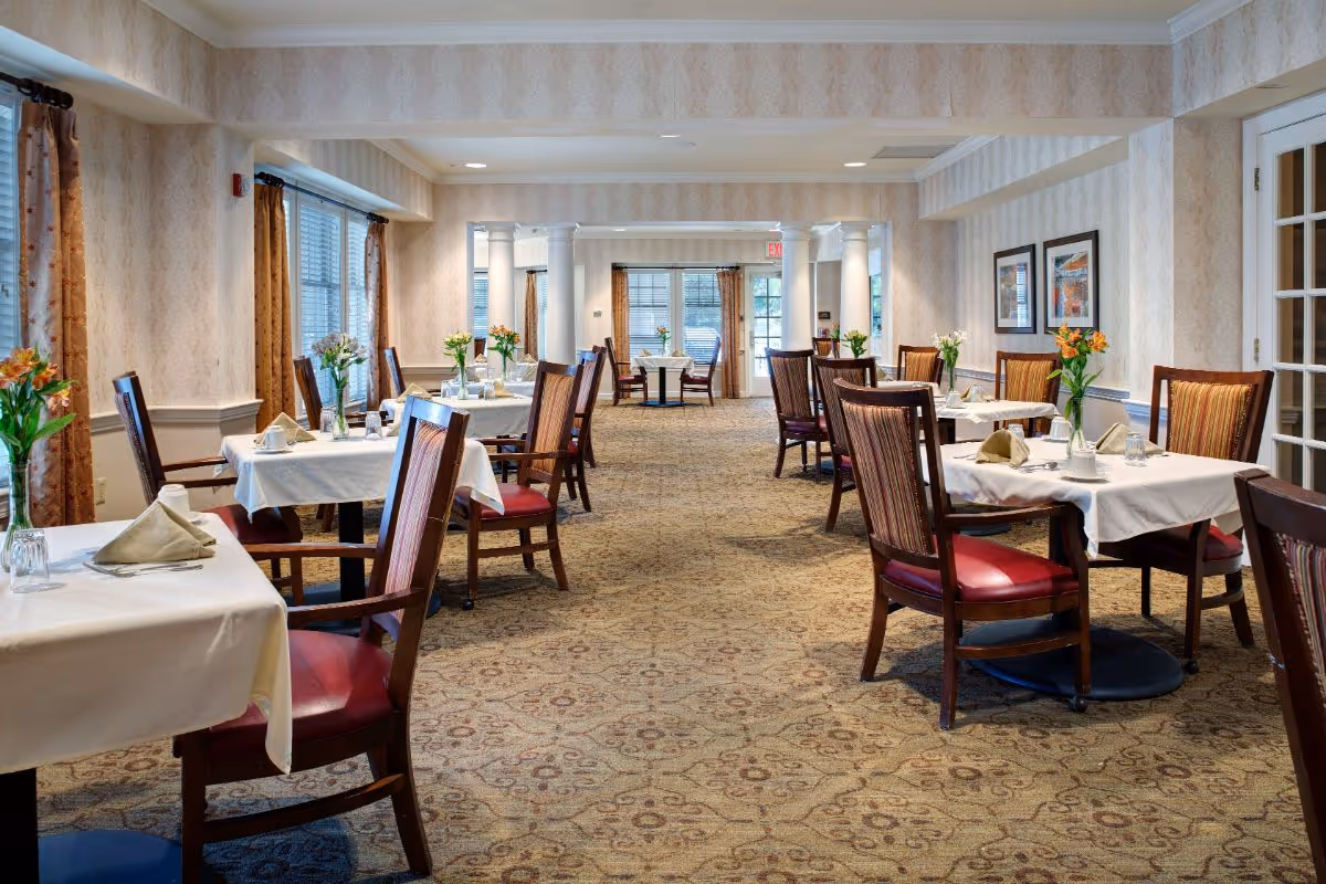 Spacious dining room with neatly set tables, upholstered chairs, and floral centerpieces.