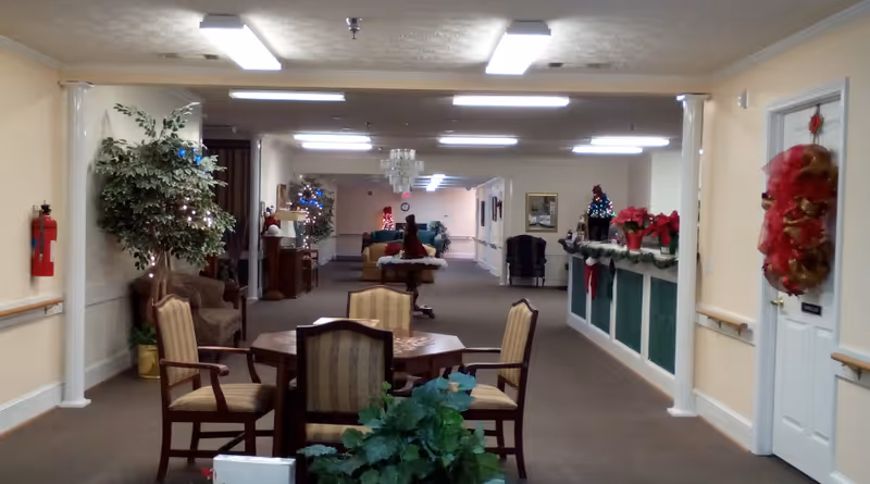 Interior common area and hallway of an assisted living facility with seating, tables, plants and holiday decorations.