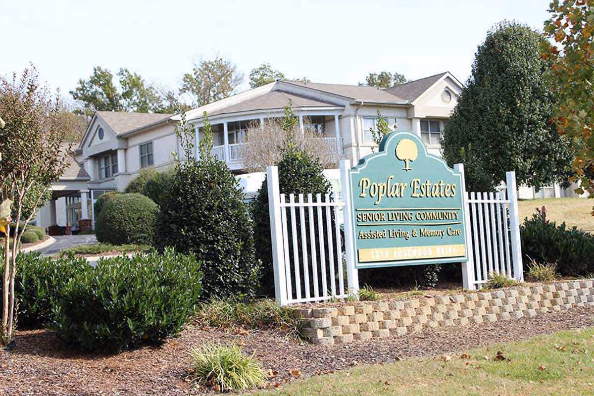 Sign for Poplar Estates with white fence and landscaping in front of the senior living building.