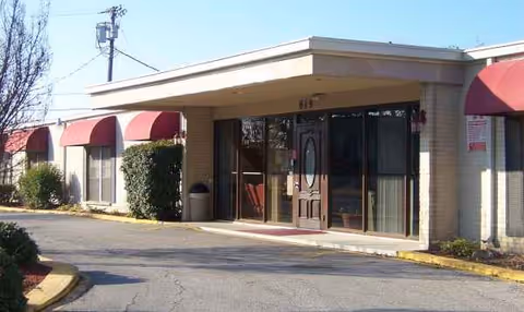 Exterior view of a single-story senior living facility entrance with maroon awnings.