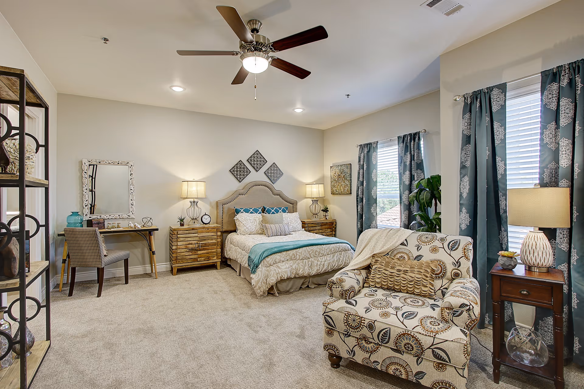 Bright, well-decorated bedroom with a bed, nightstands, desk, patterned armchair, and teal curtains.