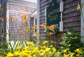 Front of Rosewood Manor with wooden siding, yellow flowers, and a green sign.