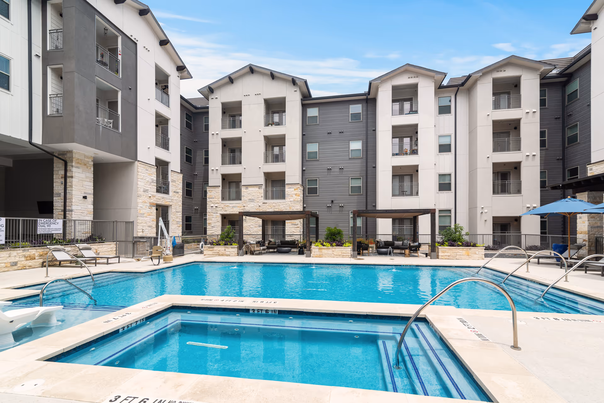 Outdoor courtyard with a swimming pool and attached spa surrounded by a multi-story apartment building and poolside seating.