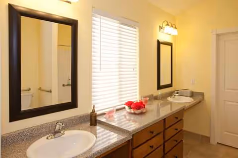 Bright bathroom with double sinks, two mirrors, and a window.
