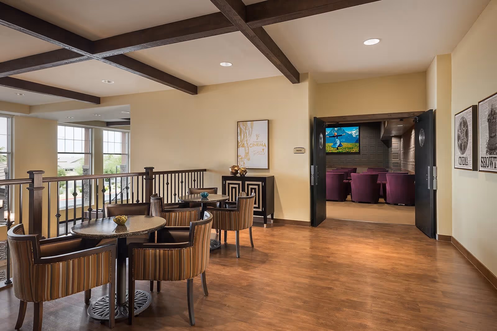 Bright communal seating area with round tables and striped chairs overlooking a lower level and a doorway into a small theater with purple seats.