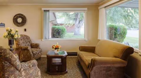 Cozy senior living lounge with sofas, chairs, a coffee table, and a large window.