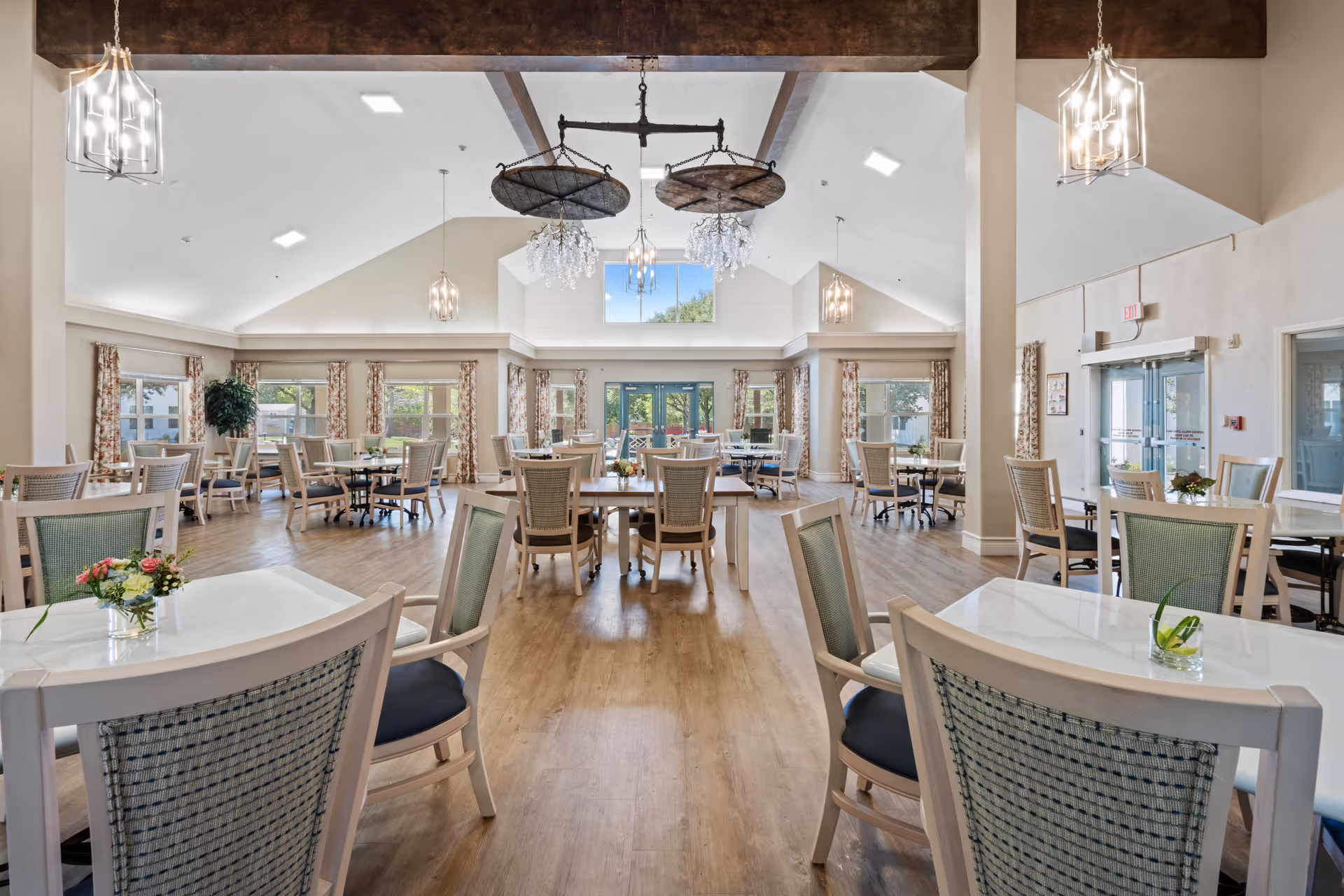 Bright, spacious dining room with multiple tables and chairs under a vaulted ceiling and large windows.
