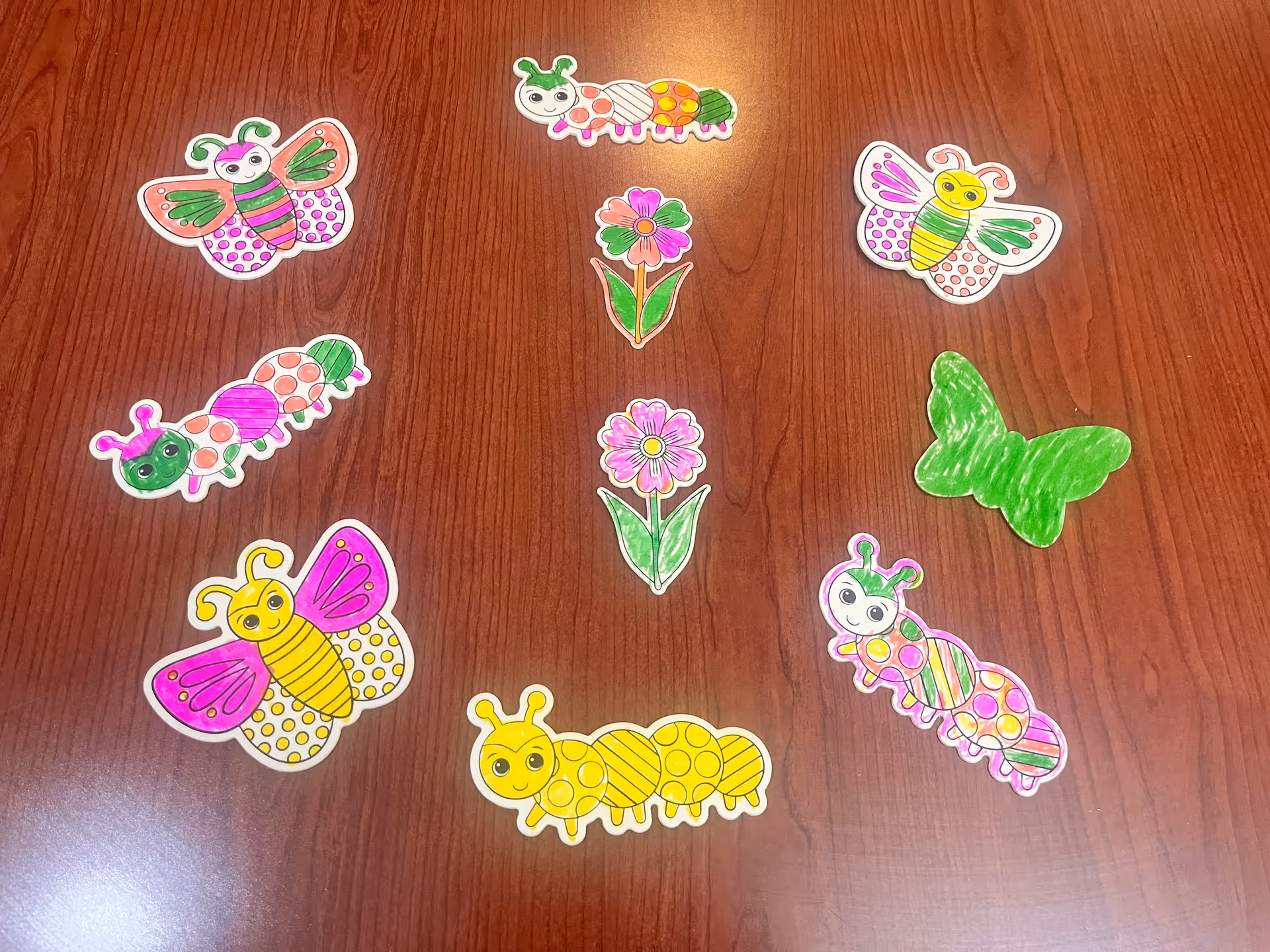Colored paper cutouts of butterflies, caterpillars, and flowers arranged on a wooden table.