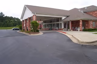 Front entrance of a brick senior living building with a covered drive-up canopy, benches, and a parked car.