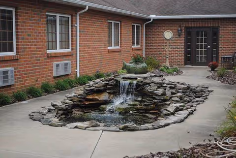 Exterior of Magnolia Terrace Assisted Living with a stone-pond fountain in a paved courtyard.