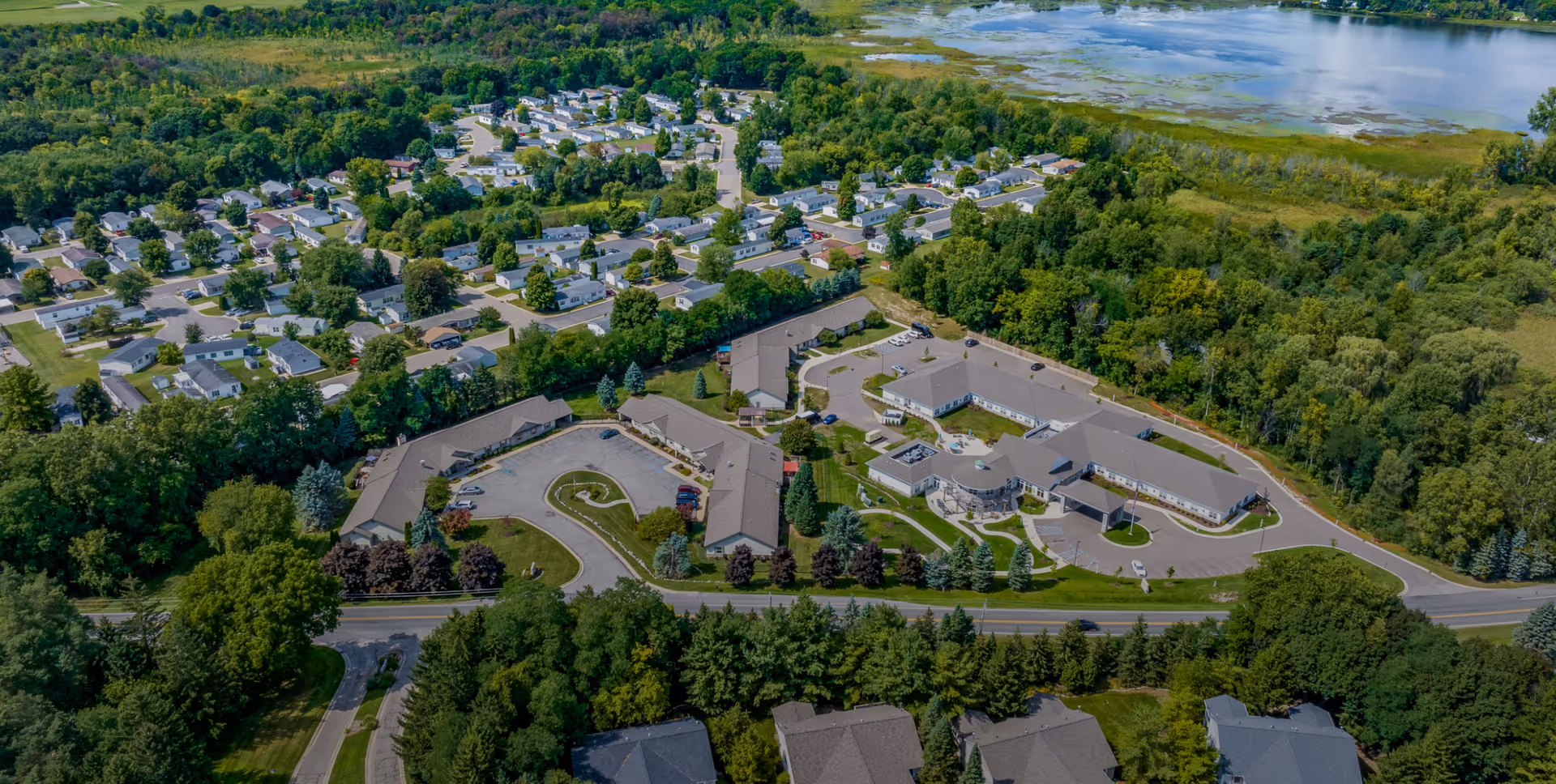 Aerial view of the Vista Springs Timber Ridge Village campus showing multiple connected buildings, circular driveways, parking areas, trees and a nearby lake.
