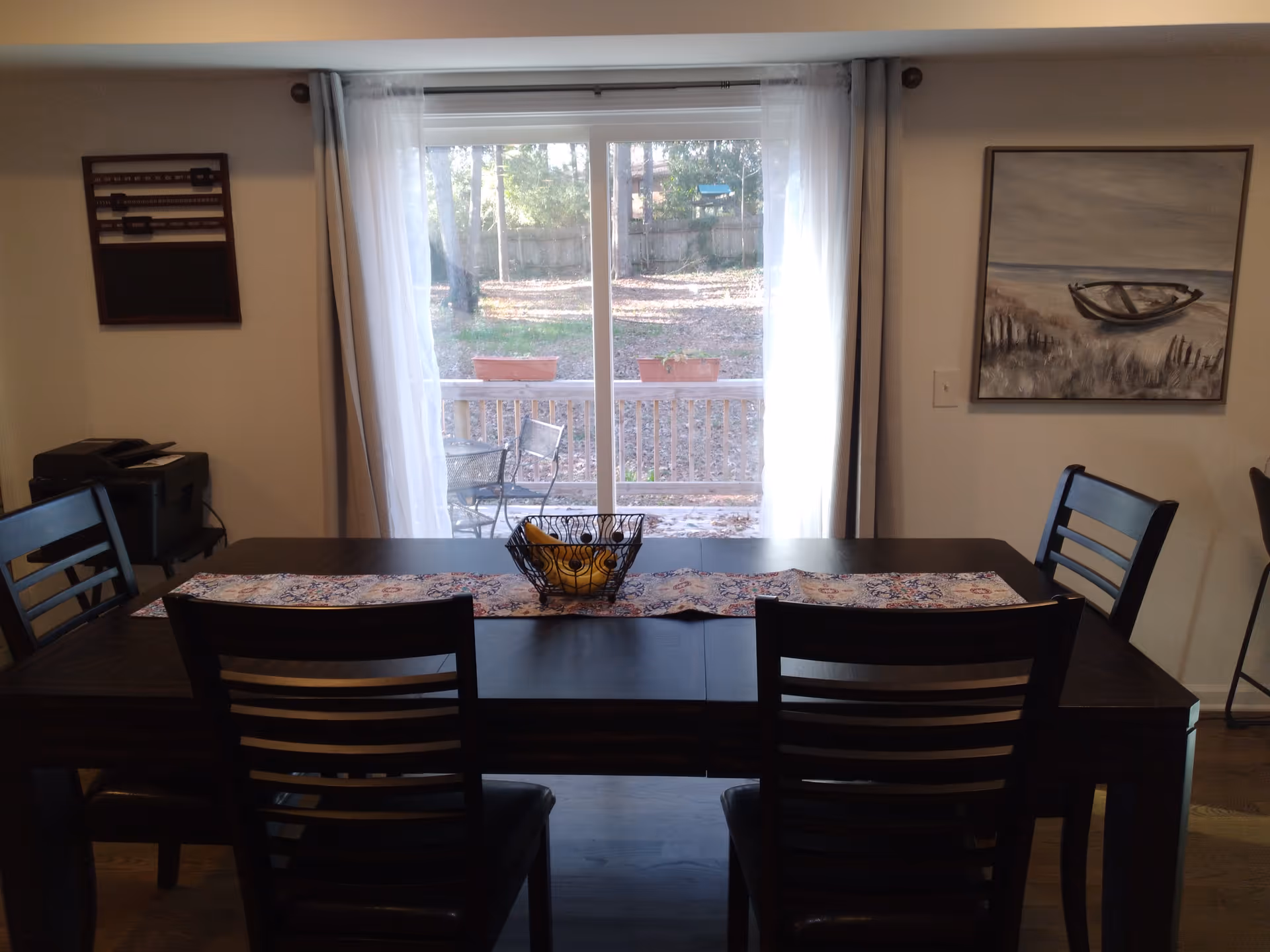 Dining room with a dark wood table and chairs facing a sliding glass door overlooking a fenced backyard.