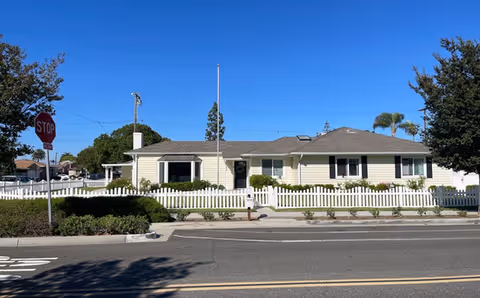 Front exterior of The Hills Senior Living, a one-story building with white siding and picket fence.