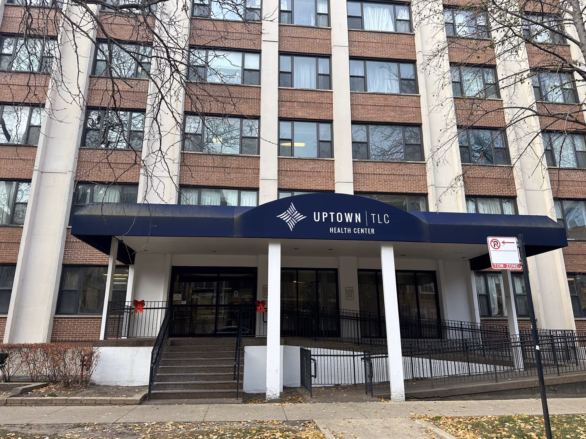 The front entrance and canopy of the Uptown TLC Health Center, a multi-story brick building with steps and a wheelchair ramp.