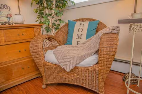 Wicker armchair with a blanket and pillow in a cozy sunlit living room corner.