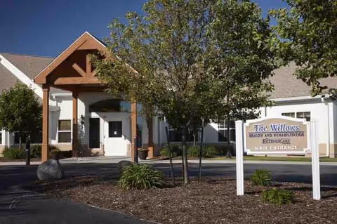 Front view of a senior living facility entrance with sign and surrounding landscaping.