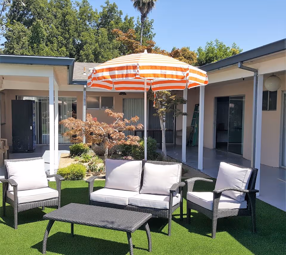 Courtyard with wicker patio seating, a striped orange-and-white umbrella, and surrounding building walkways.