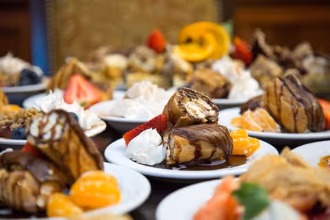 Several plated desserts with pastries drizzled in chocolate, whipped cream, and fruit slices arranged on a table.