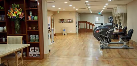Interior communal exercise space in a senior facility with treadmills and seating.