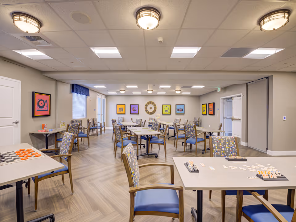 Bright multipurpose dining and activity room with tables and patterned chairs arranged for games and socializing and colorful artwork on the walls.