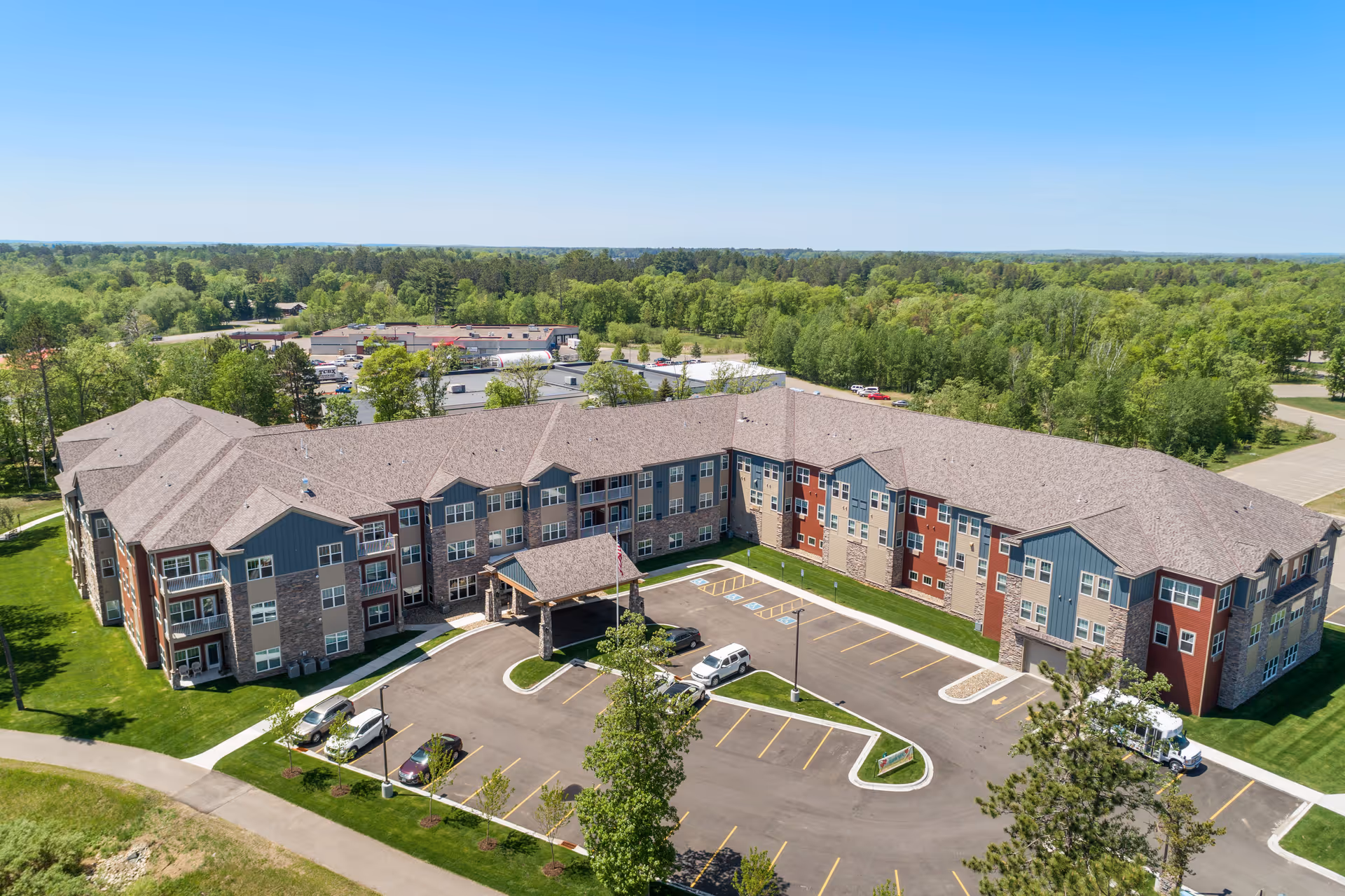 Aerial view of a large three-story senior living building with a courtyard, parking lot, and surrounding trees.