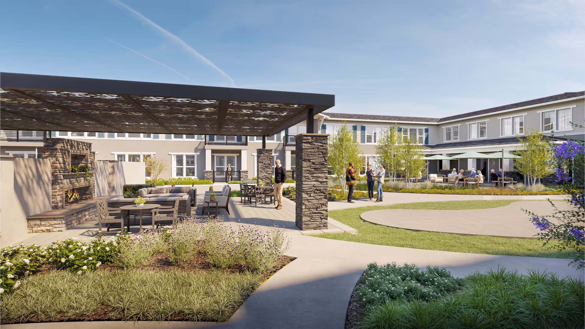 Outdoor courtyard area of The Ivy At Blue Oaks senior living facility featuring a covered seating area with a stone fireplace, several tables and chairs, landscaped garden beds, walking paths, and a two-story building in the background. People are seen standing and sitting, enjoying the outdoor space under clear blue skies.